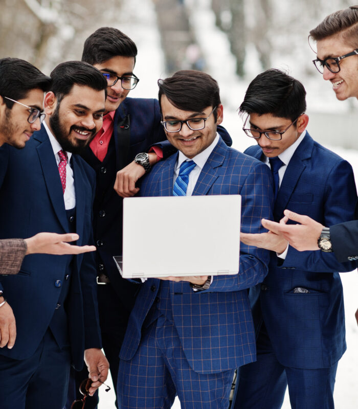 Group of six indian businessman in suits posed outdoor in winter day at Europe, looking on laptop.